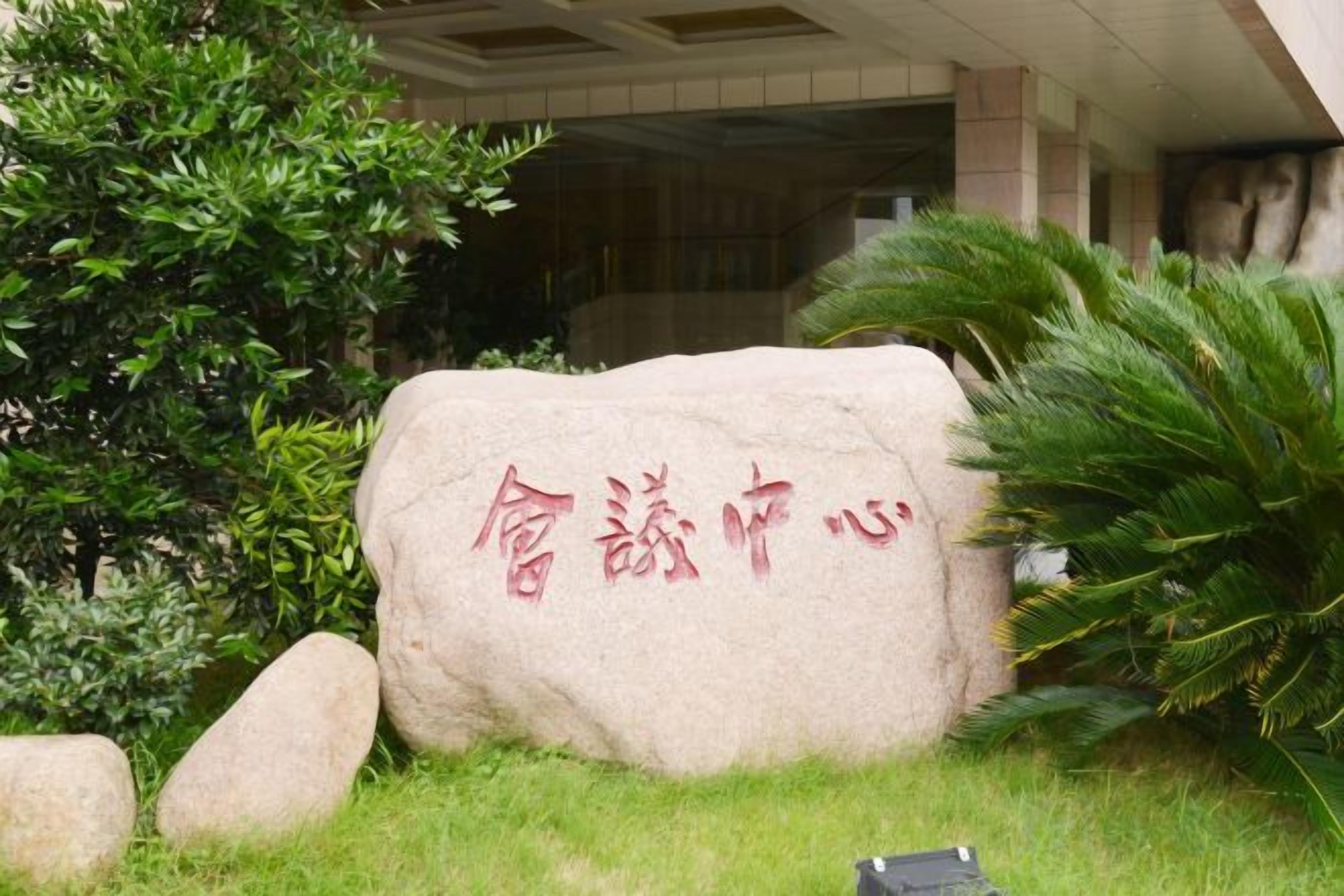 A stone with red text, surrounded by greenery and a building entrance.