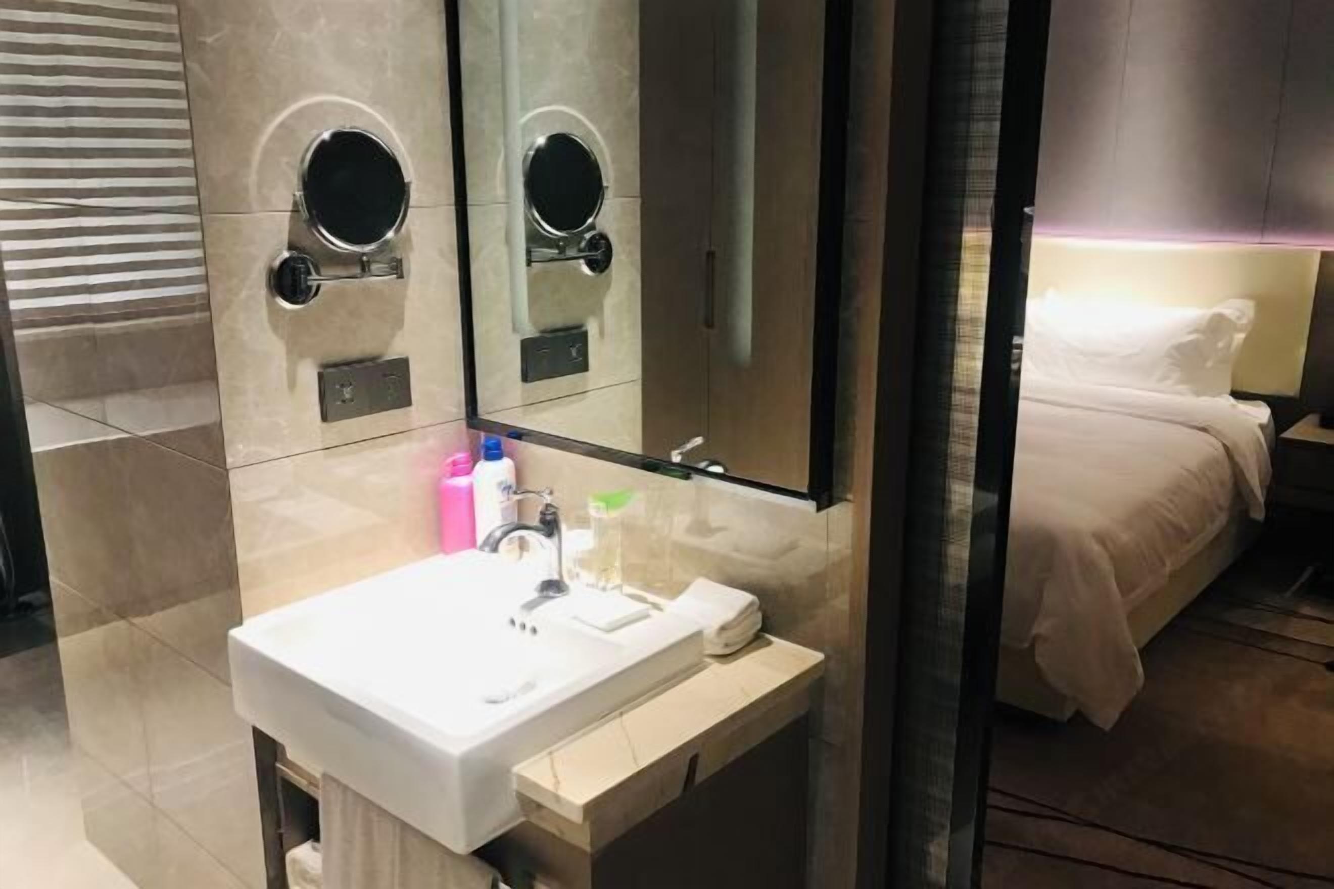 Un bagno moderno con un lavandino bianco, uno specchio e due specchietti rotondi sopra. Nell'stanza accanto, un letto con biancheria da letto bianca.