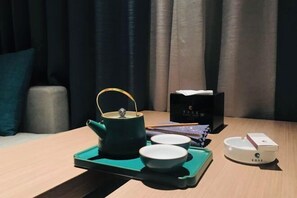 Uma mesa com uma chaleira verde, duas xícaras brancas, um suporte e uma caixa branca com tampa.