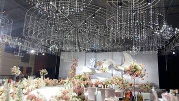 Une salle de banquet avec des tables rondes, des centres de table floraux et un grand lustre.