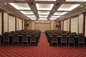 Un salón de conferencias con filas de mesas y sillas, piso cubierto de alfombra roja y un techo alto con iluminación empotrada.