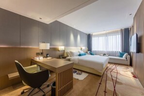 Quarto de hotel moderno com uma cama grande, uma escrivaninha, uma cadeira e uma televisão.