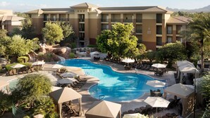Un hotel con piscina rodeada de sillas de descanso y sombrillas, con montañas al fondo.