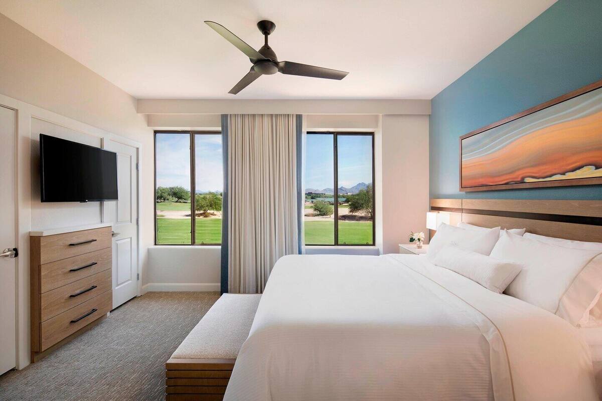 Een hotelkamer met een bed, een televisie, een plafondventilator, een schilderij en uitzicht op een golfbaan.