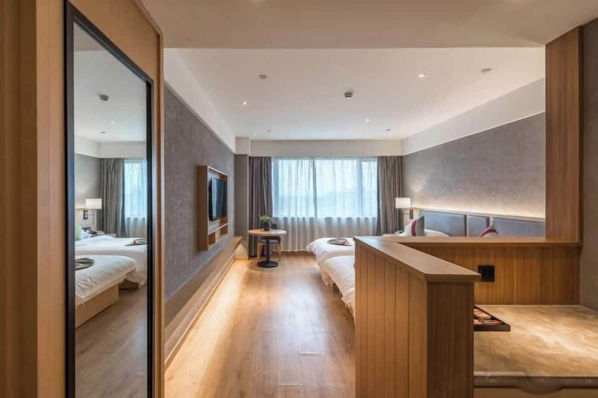A hotel room with a wooden floor, a bed, a desk, a chair, a TV, and a window with curtains.