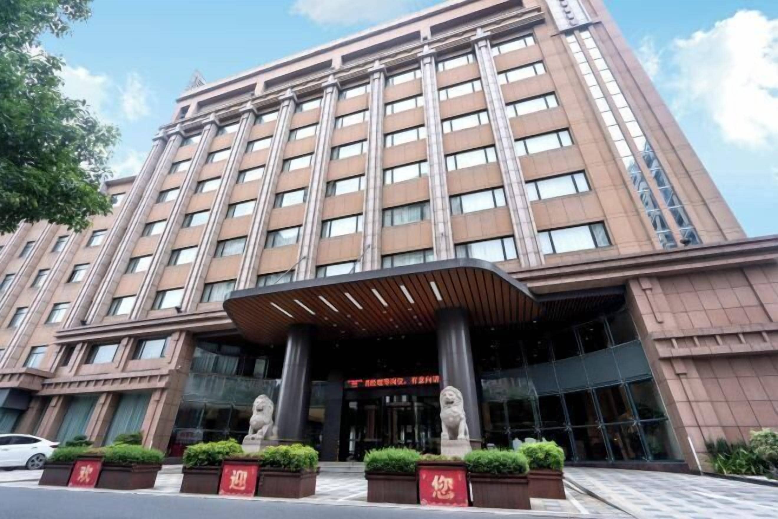 A multi-story hotel with a modern facade, large windows, and a prominent entrance with a covered area and statues.