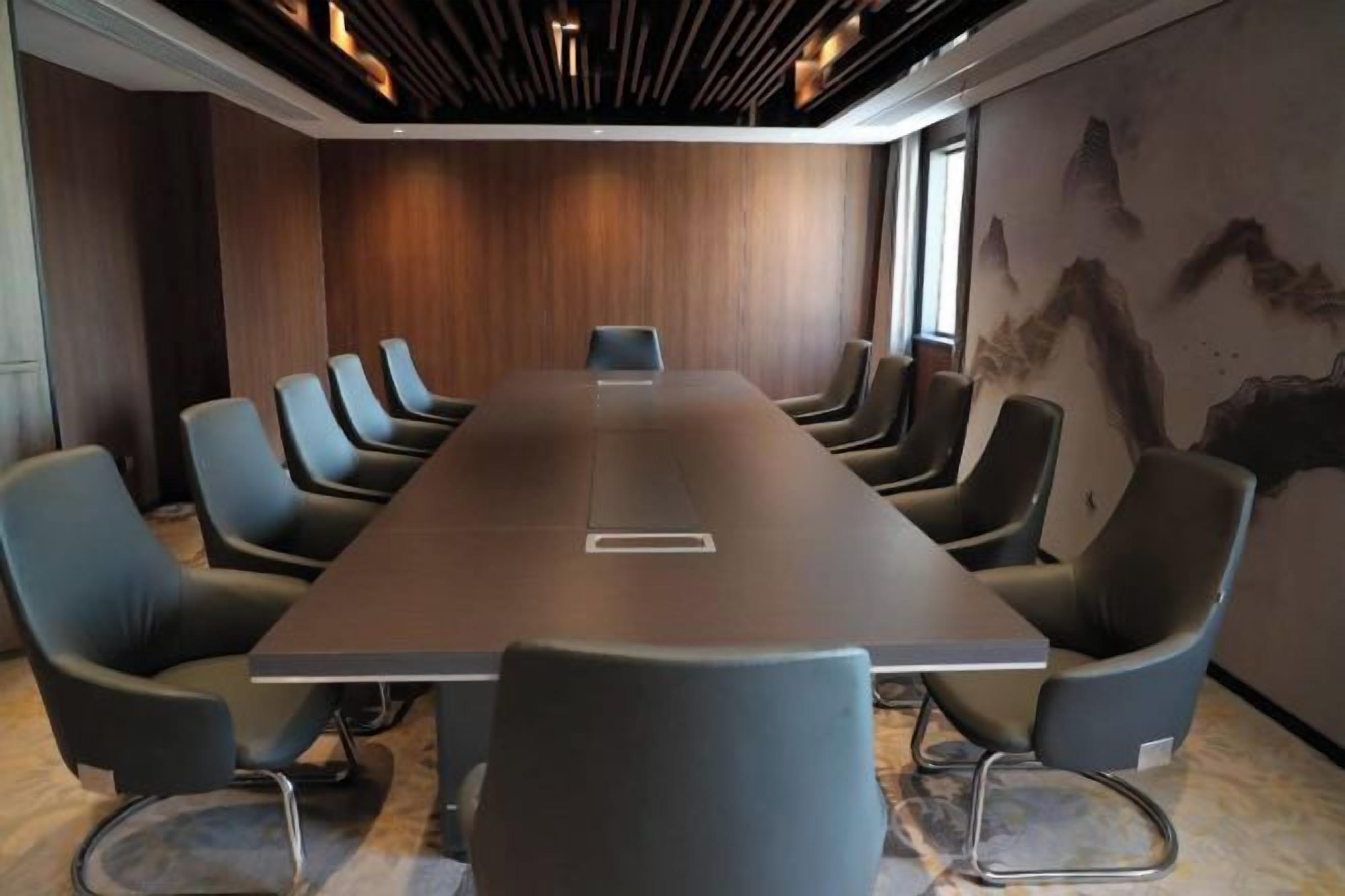 Un salón de conferencias con una larga mesa y numerosas sillas, paneles de madera en las paredes y un amplio ventanal.