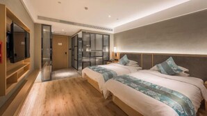Una habitación de hotel moderna con dos camas, un televisor y un baño con paredes de vidrio.