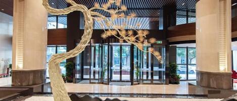 A lobby with a large tree sculpture, a reception desk, and a glass entrance.