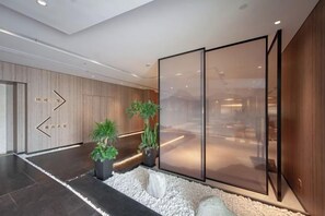 A modern hotel lobby with a reception desk, directional signs, and potted plants. - Shengxiao Grand Hotel (Quzhou Airport) (Quzhou)
