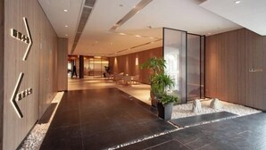 Un moderno vestíbulo de hotel con piso de baldosas oscuras, paneles de madera y una gran planta en maceta.