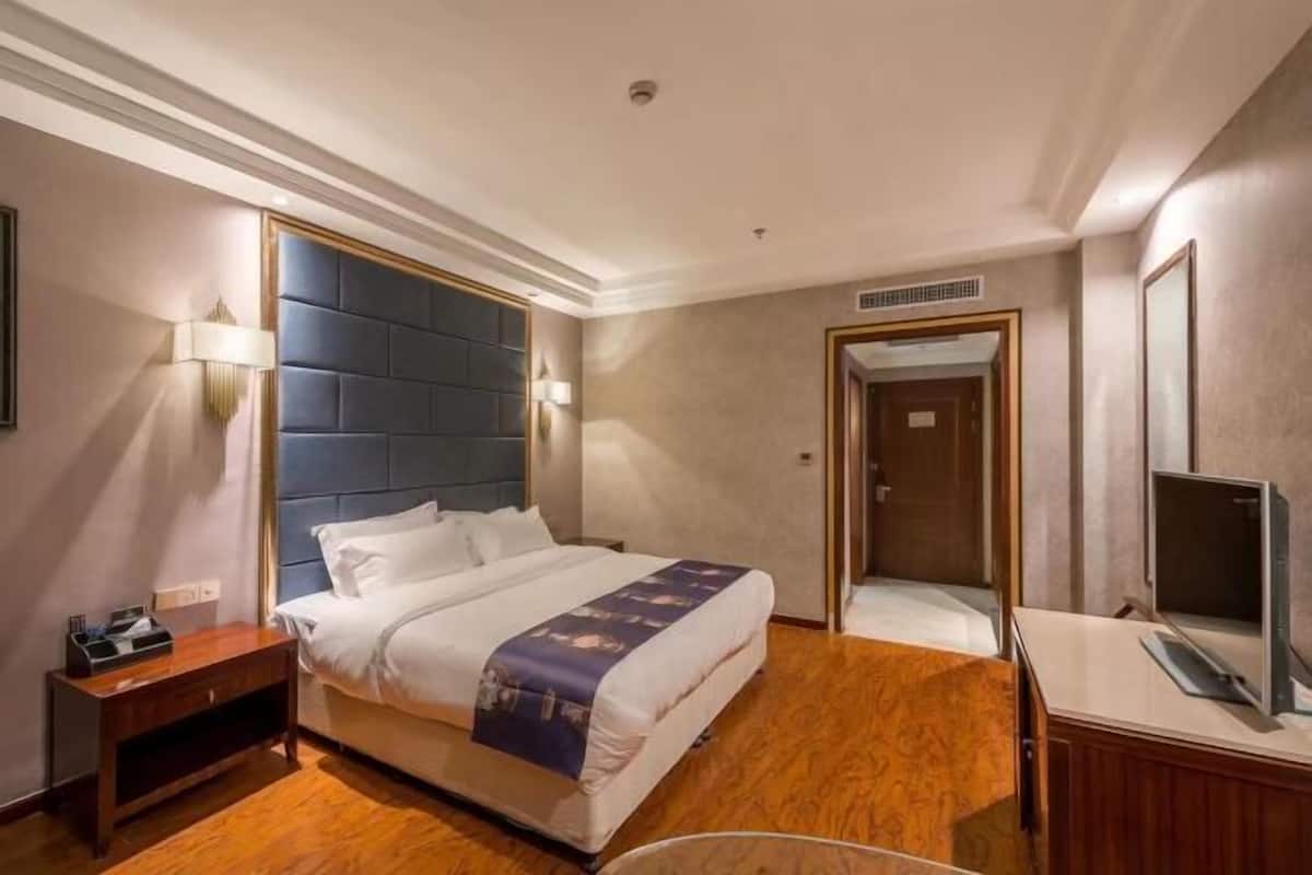 A hotel room with a bed, bedside table, lamp, TV, and a door leading to another room.