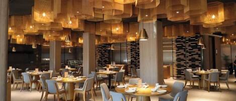 A restaurant with round tables, chairs, hanging wooden light fixtures, and a bookshelf in the background.