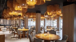 Un comedor moderno con mesas y sillas redondas, detalles de madera e iluminación colgante.