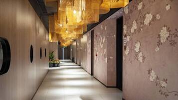 A corridor with a wooden wall, a floral wallpapered wall, and hanging lights.
