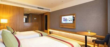 Habitación de hotel con dos camas, una mesita, una silla y un televisor montado en la pared.