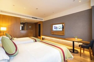 Habitación de hotel con dos camas, una mesita, una silla y un televisor montado en la pared.