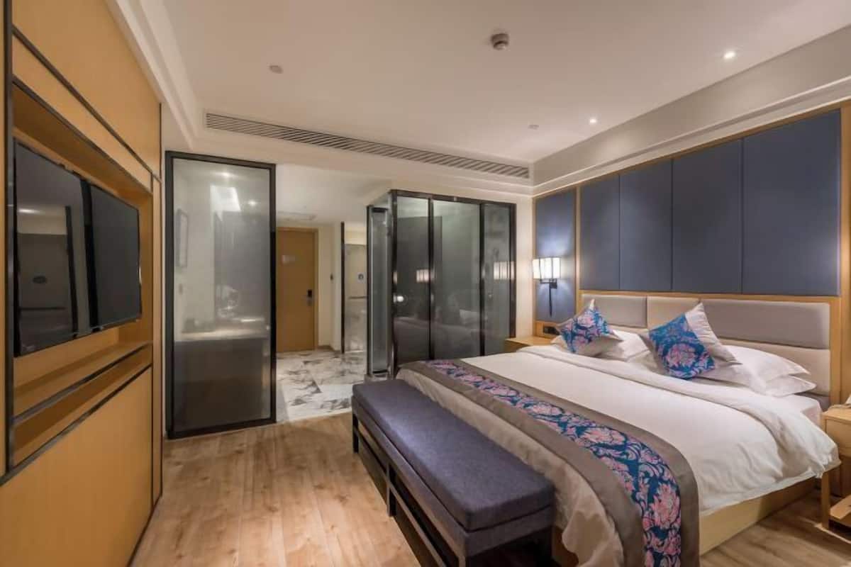 A modern hotel room with a large bed, a bench, a TV, and a wardrobe.