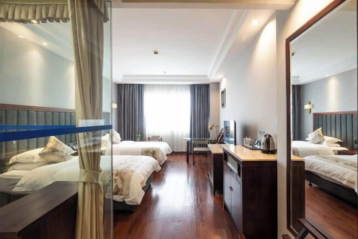 A hotel room with two beds, a desk, a chair, a mirror, and a window with curtains.