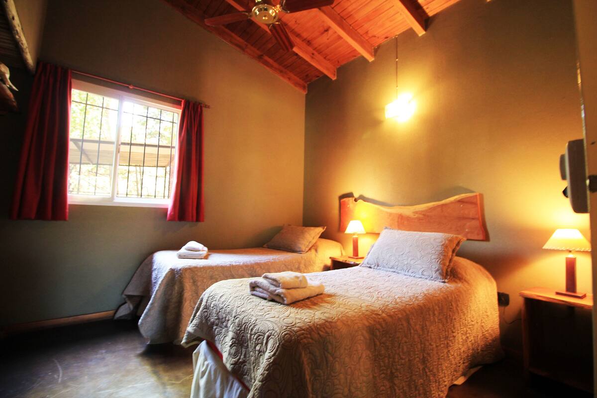 A room with two beds, a window with red curtains, and a ceiling fan.