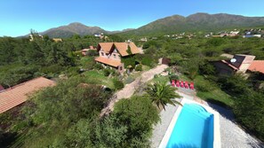 Zona residencial con piscina, sillas de descanso rojas y montañas al fondo.