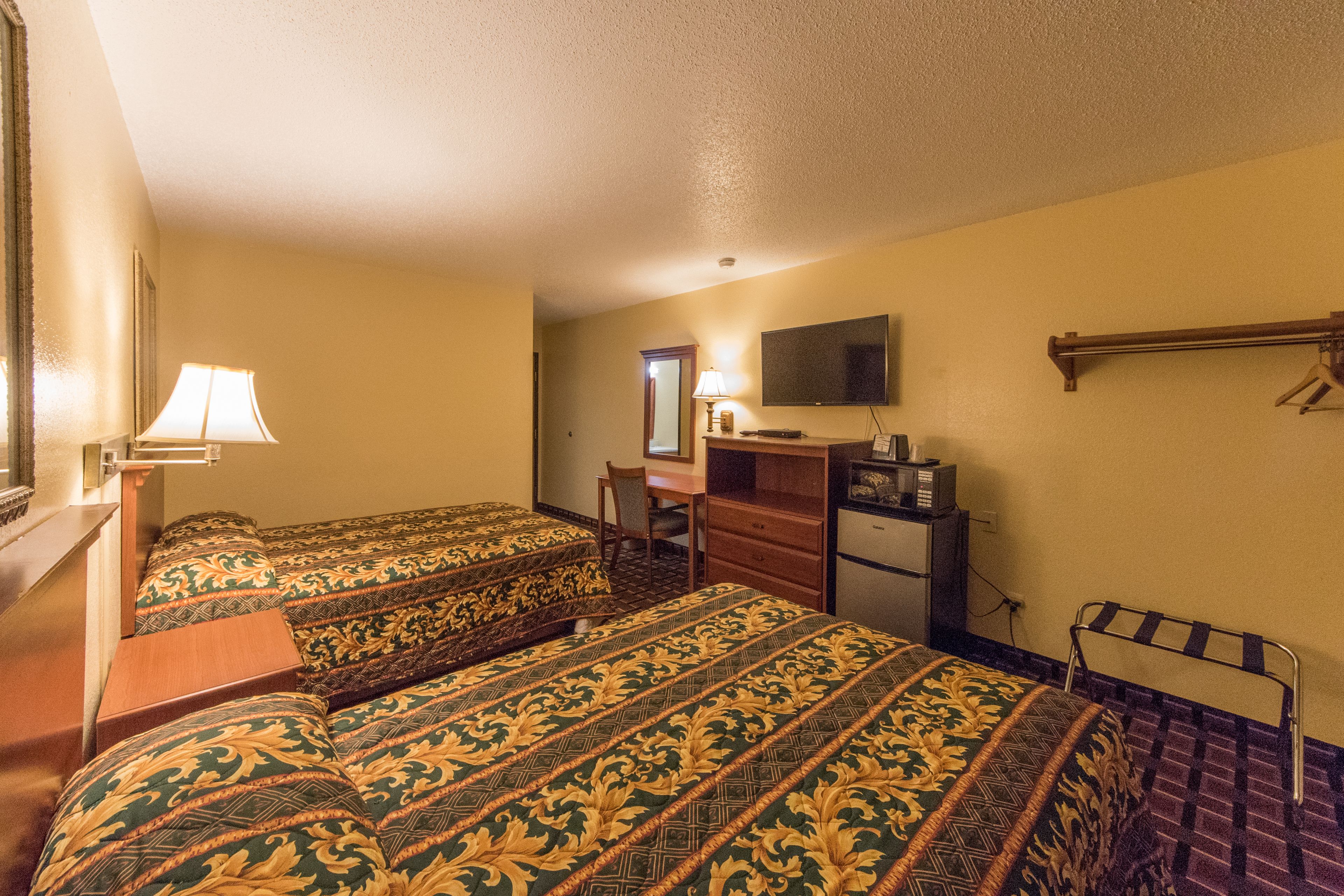 A hotel room with two beds, a desk, a chair, a television, and a wardrobe.