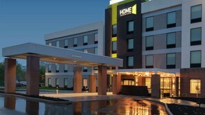 Un hotel moderno con un grande cartello che riporta "HOME 2", un ingresso coperto e una piscina a specchio.