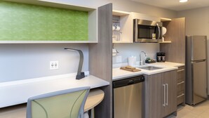 Una cucina moderna con lavastoviglie integrata, elettrodomestici in acciaio inossidabile e un piccolo angolo ristoro con una sedia.