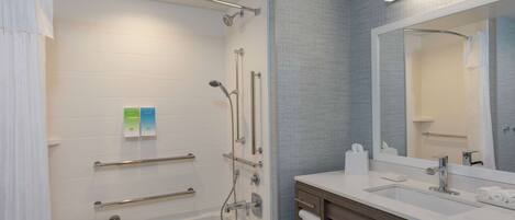Une salle de bain moderne dotée d’une douche à l’italienne, de barres d’appui, d’une baignoire, d’un meuble-lavabo avec miroir et d’un porte-serviettes.