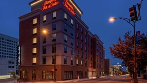 A multi-story hotel with illuminated signage, a brick facade, and a street view with traffic lights and trees.