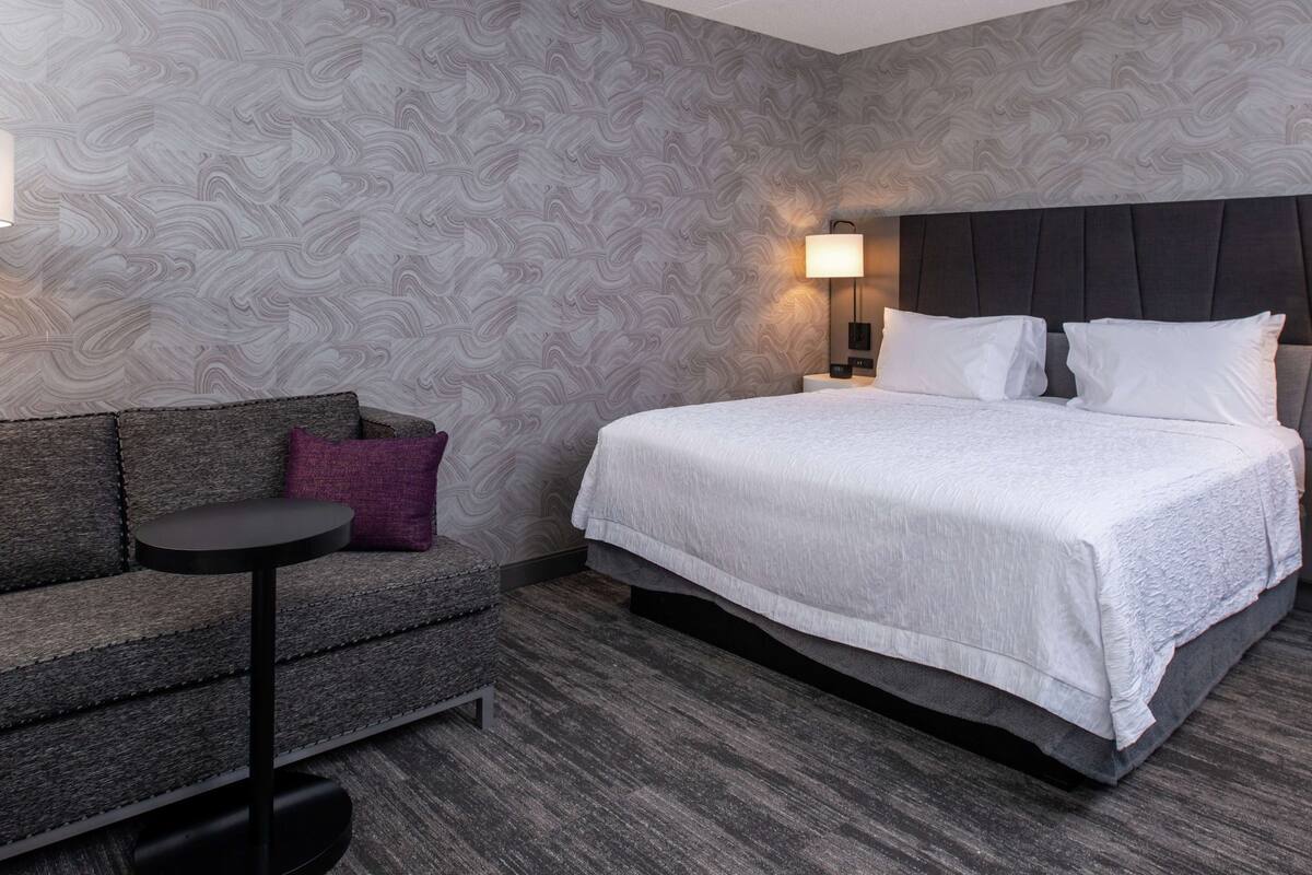 A hotel room with a bed, a sofa, a small table, and a wall with a patterned wallpaper.