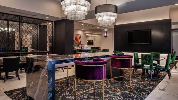 A modern bar area with a marble countertop, purple bar stools, and a large chandelier.
