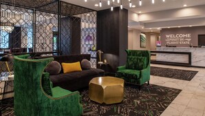 A modern lobby with a reception desk, green upholstered seating, and a geometric-patterned floor.