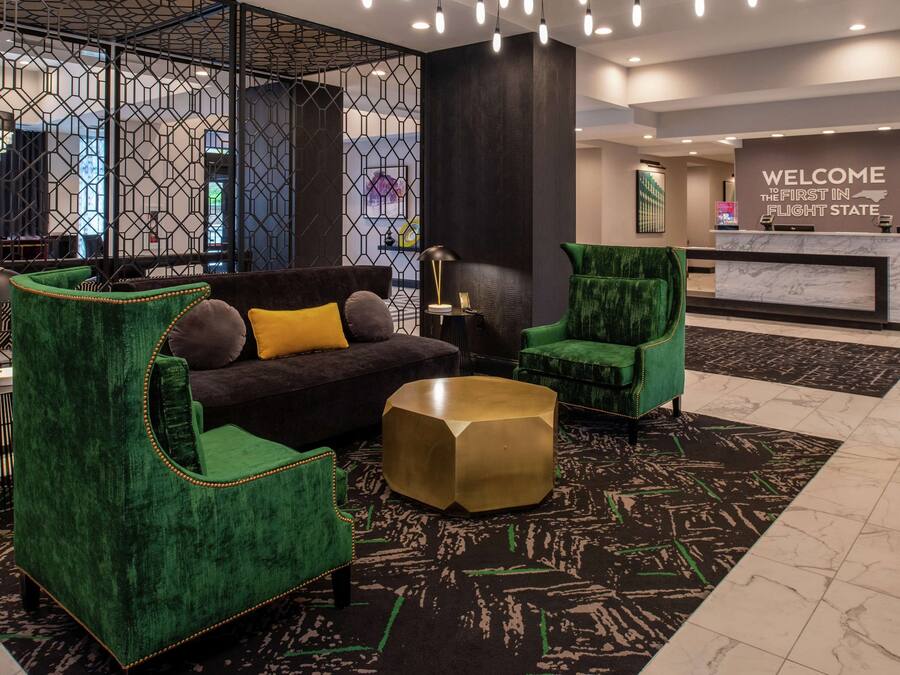 Un vestíbulo moderno con un mostrador de recepción, asientos tapizados en verde y un suelo con estampado geométrico.