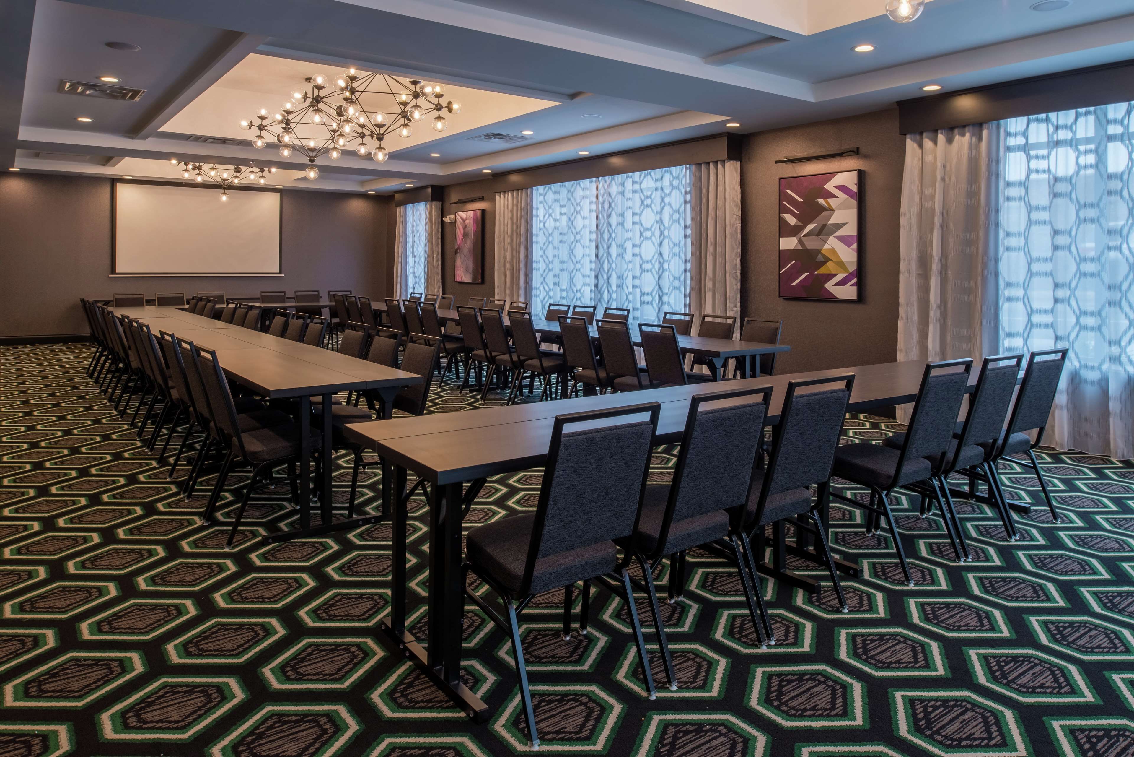 A conference room with a long table, chairs, a projector screen, and a patterned carpet.
