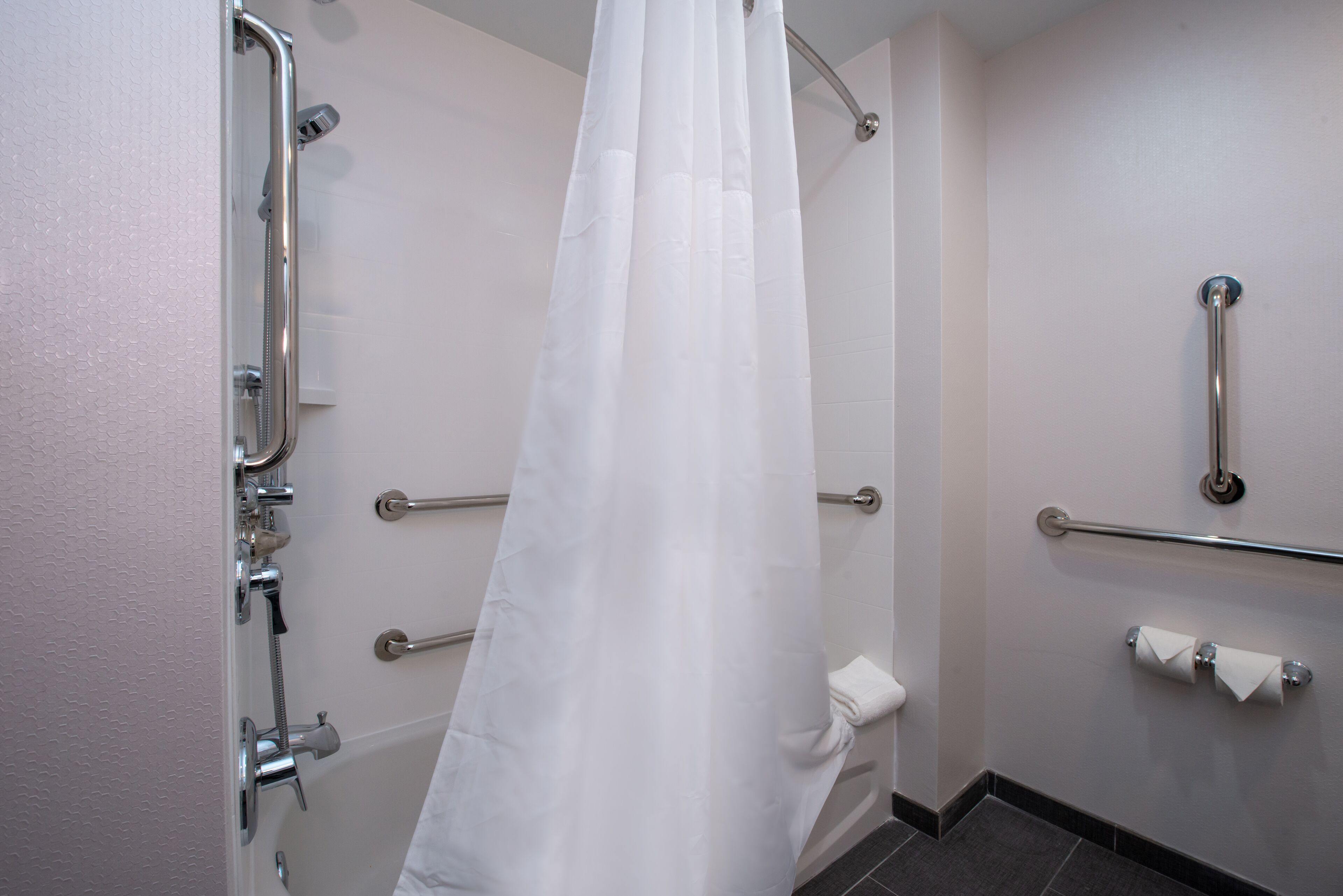 A bathroom with a shower, grab bars, and a toilet.