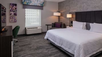 Habitación de hotel con una cama grande, un escritorio, una silla, un ventanal con persianas, un aire acondicionado de pared y dos lámparas de pared.