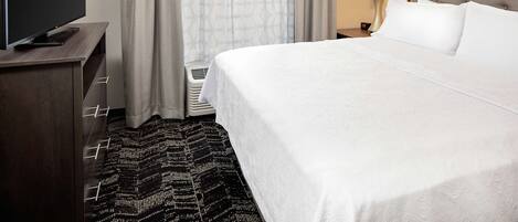 Una camera d'albergo con un letto, una televisione, una lampada e una finestra con tende.