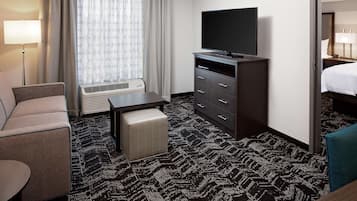A hotel room with a sofa, a small table, a TV on a stand, a dresser, and a bed.