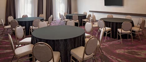 A conference room with round tables and chairs, a flat-screen TV, and a large window with curtains.
