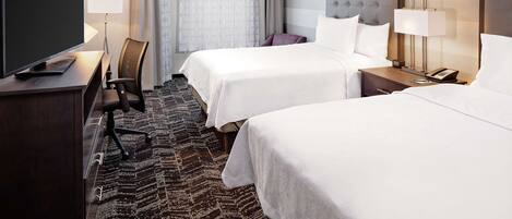 A hotel room with two beds, a desk with a TV, a chair, a lamp, and a telephone.
