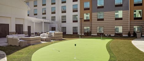 A courtyard with a putting green, outdoor seating, and a multi-story building with large windows.