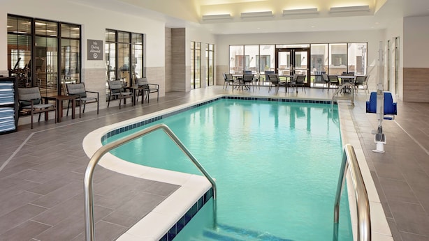 Une piscine intérieure à l’eau d’un bleu limpide, entourée de chaises longues et de tables.