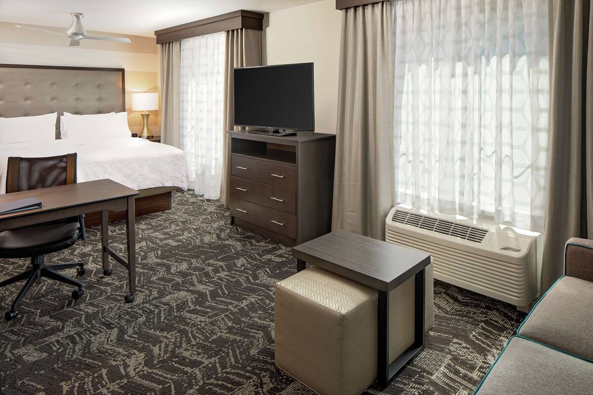 Ein Hotelzimmer mit Bett, Schreibtisch mit Stuhl, Fernseher, Heizung und einem Fenster mit Vorhängen.