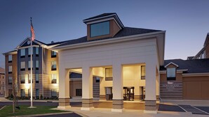 L’entrée d’un hôtel, avec un drapeau, une allée couverte et une enseigne indiquant « Homewood Suites Hilton ».