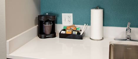 A kitchen counter with a coffee maker, a box of tissues, and a paper towel dispenser.