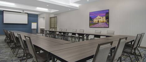 Une salle de conférence avec une longue table, des chaises, un écran de projection et un tableau accroché au mur.