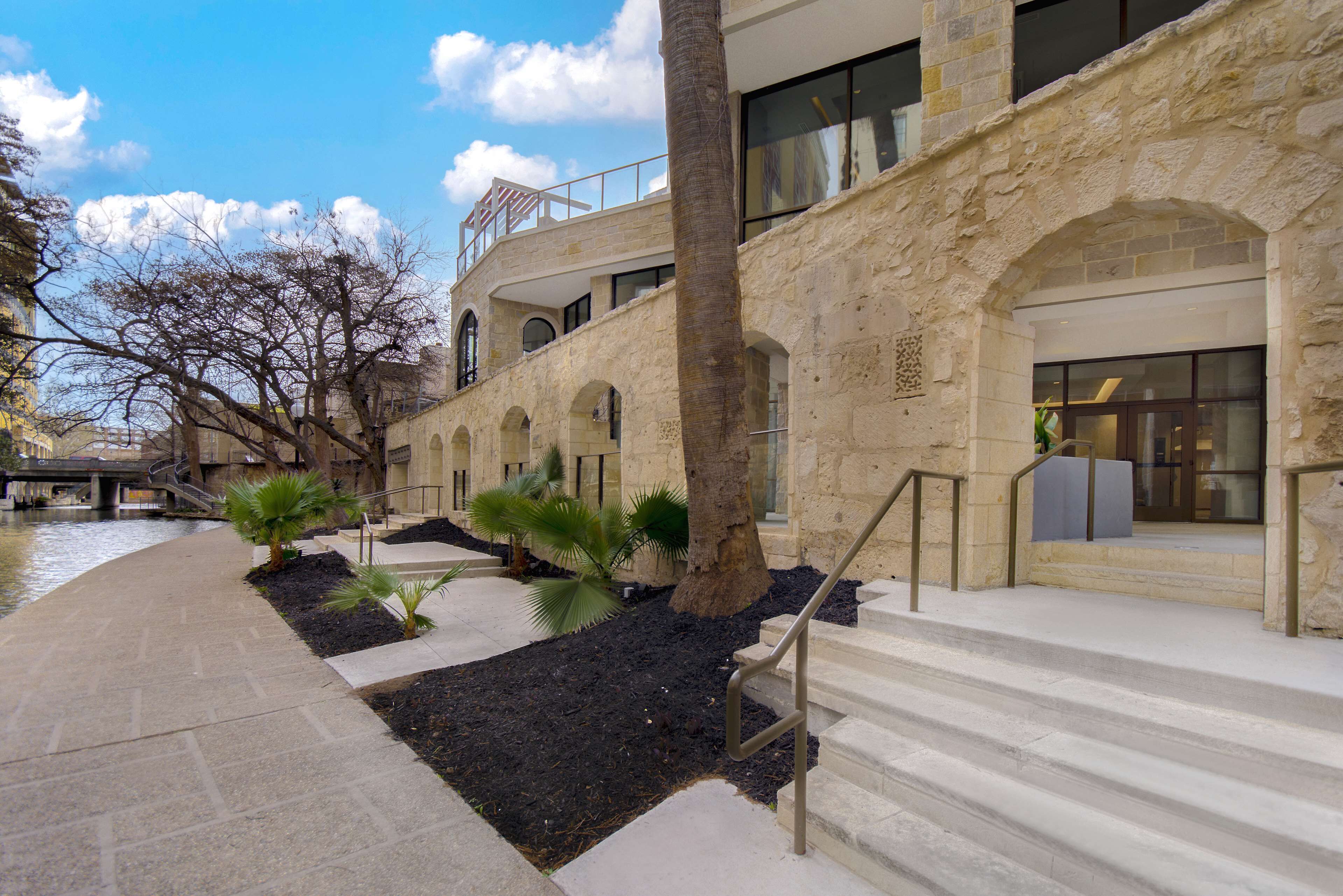 Un edificio de piedra con ventanas de arco y una palmera en el patio.