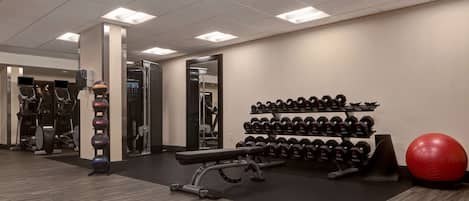 Un gimnasio con equipo de ejercicio, una banca, una pared de mancuernas y una pelota de ejercicios roja.