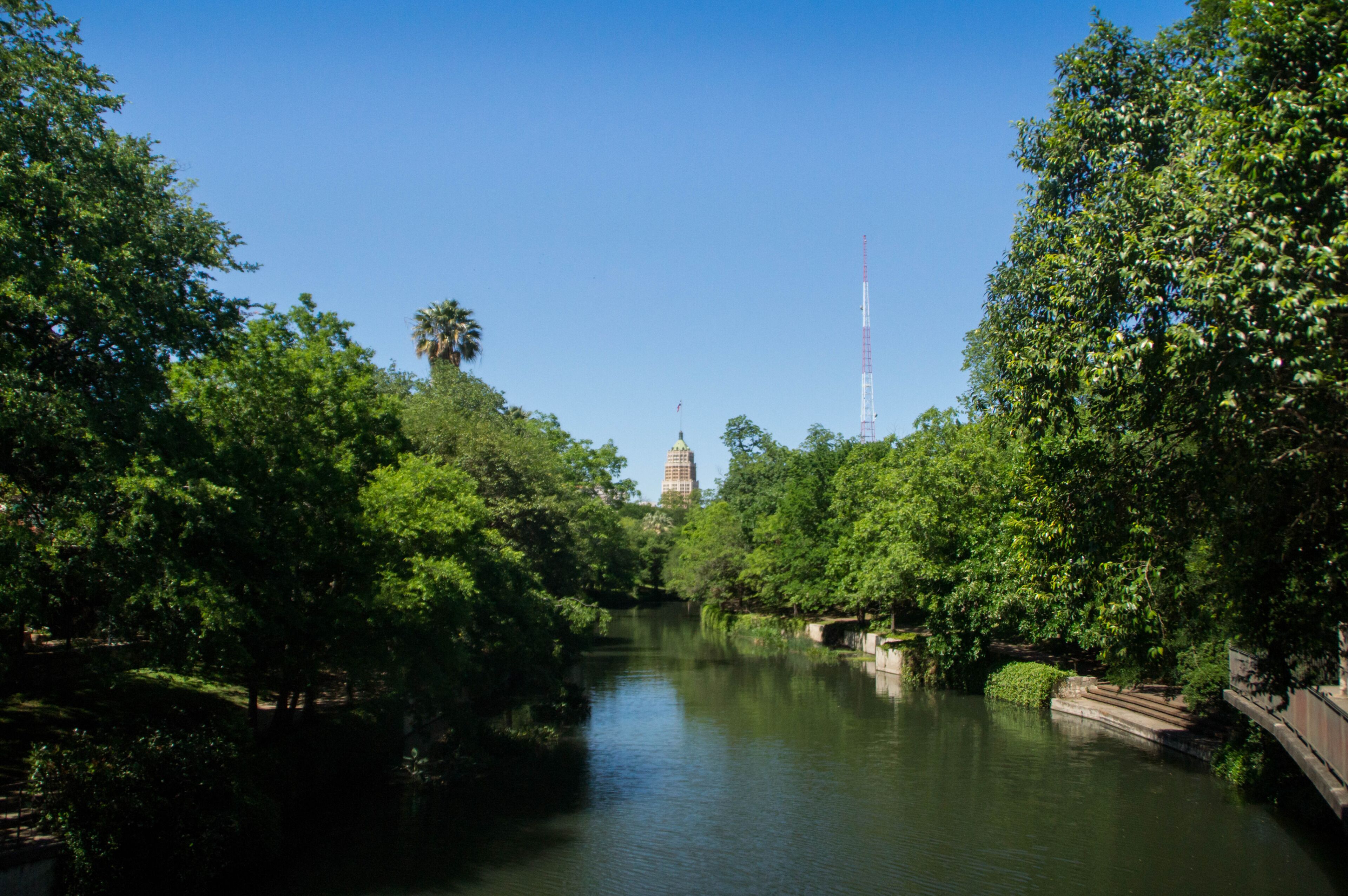 A river with trees on both sides, a bridge, and a tower in the background.